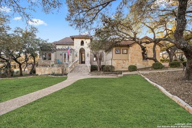 mediterranean / spanish home featuring stone siding, stucco siding, a tile roof, and a front lawn