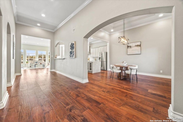 interior space with baseboards, visible vents, dark wood finished floors, arched walkways, and crown molding