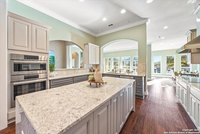 kitchen featuring light stone counters, a kitchen island, double oven, and dark wood-style floors