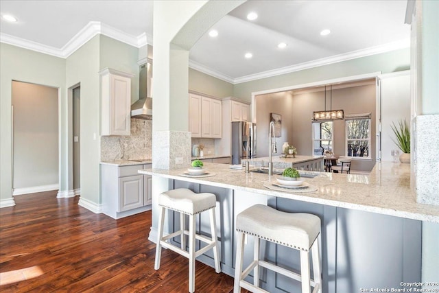 kitchen featuring wall chimney range hood, stainless steel fridge with ice dispenser, arched walkways, a peninsula, and dark wood-style floors