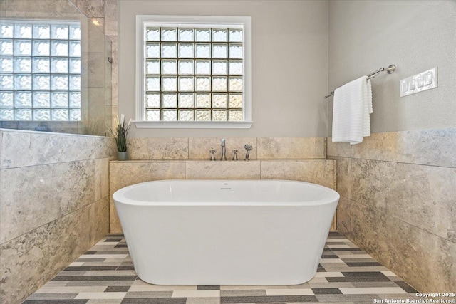 bathroom with a wainscoted wall, a freestanding bath, and tile walls