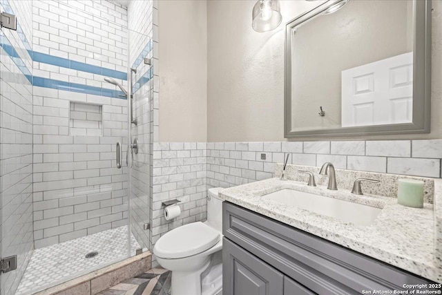 full bathroom with vanity, a wainscoted wall, a stall shower, tile walls, and toilet