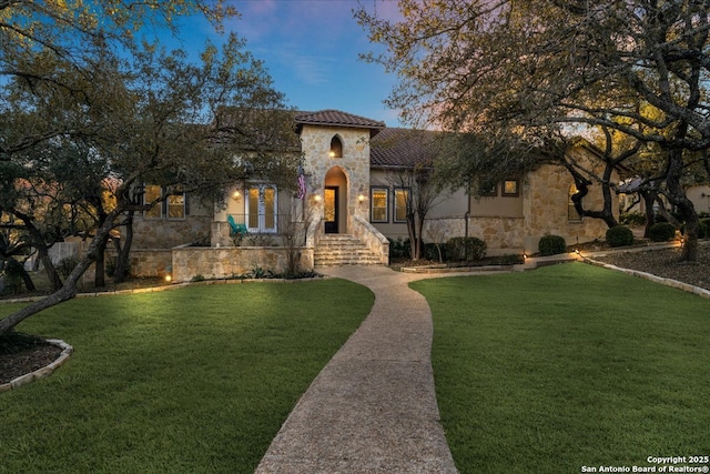 mediterranean / spanish-style house with stone siding, stucco siding, and a front yard