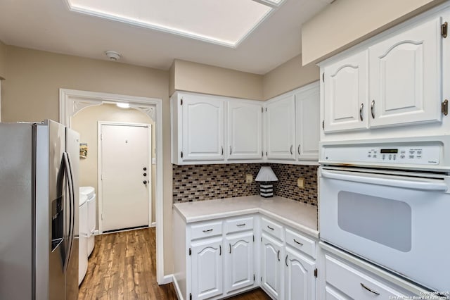 kitchen with washing machine and clothes dryer, stainless steel refrigerator with ice dispenser, white cabinetry, white oven, and backsplash