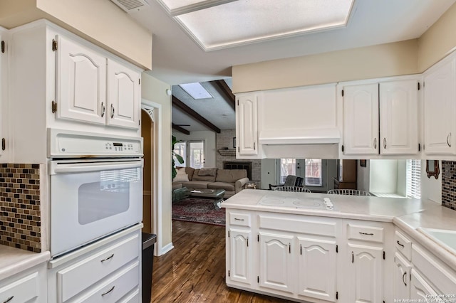 kitchen with dark wood finished floors, white cabinetry, white appliances, a skylight, and decorative backsplash