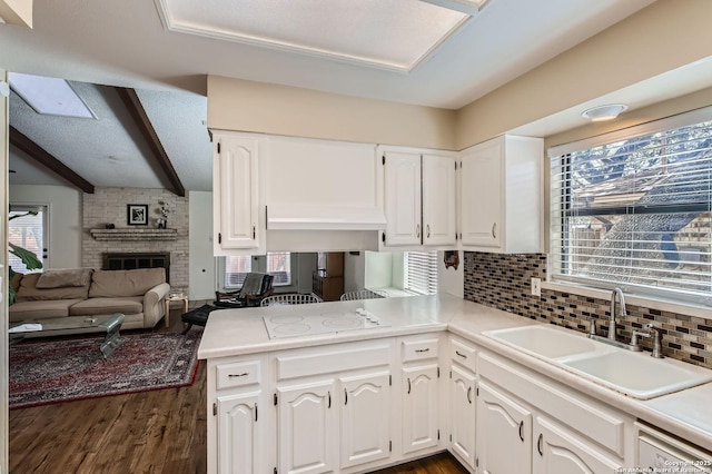 kitchen featuring tasteful backsplash, a stone fireplace, white cabinets, and a sink