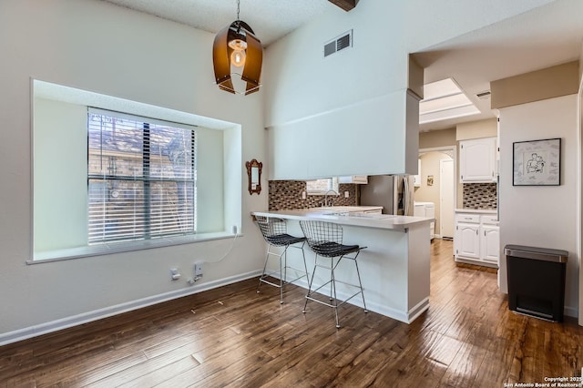 kitchen featuring visible vents, a kitchen bar, white cabinetry, stainless steel fridge, and a peninsula