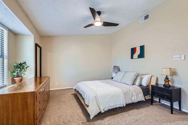 bedroom featuring visible vents, baseboards, light carpet, a textured ceiling, and a ceiling fan