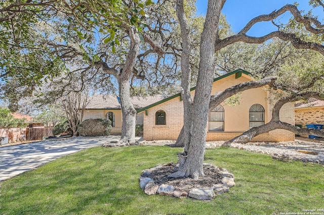 view of front of property featuring brick siding, fence, a front yard, stucco siding, and driveway