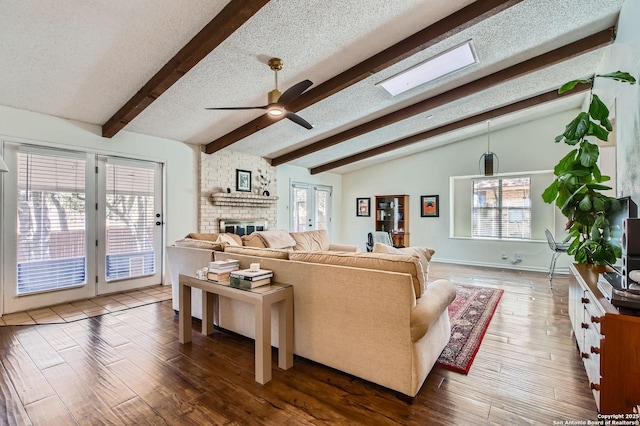 living room featuring a ceiling fan, lofted ceiling with beams, a textured ceiling, wood finished floors, and a fireplace