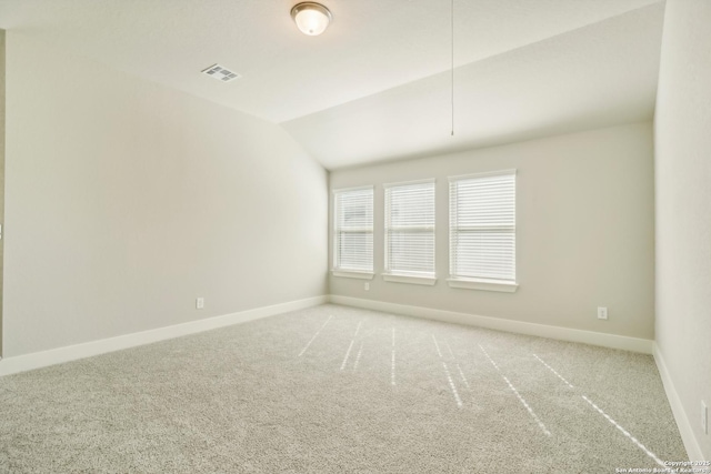 carpeted empty room with vaulted ceiling, attic access, baseboards, and visible vents