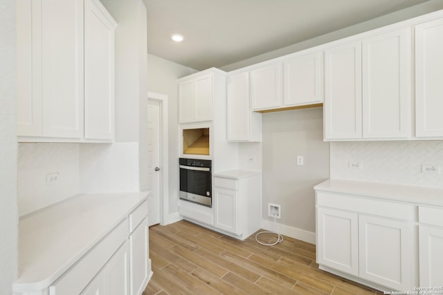 kitchen featuring white cabinetry, backsplash, wall oven, and wood finish floors