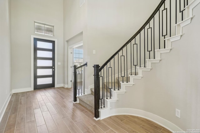 entryway with visible vents, baseboards, wood tiled floor, stairs, and a towering ceiling