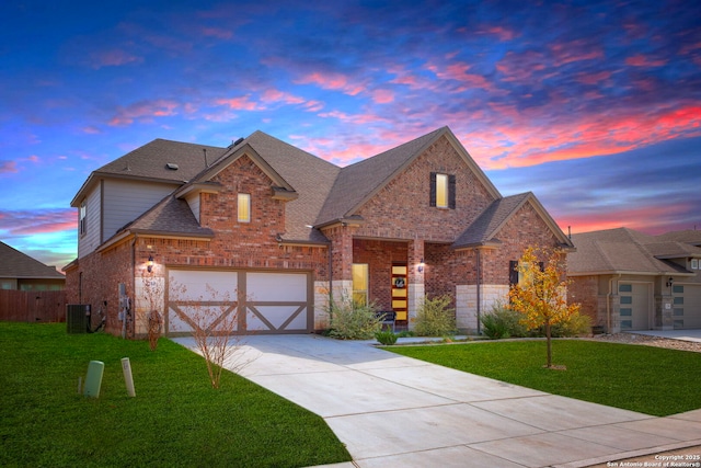 view of front of house with central air condition unit, brick siding, a garage, and a lawn