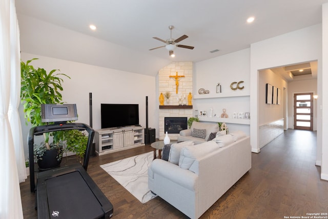 living area featuring visible vents, a ceiling fan, a fireplace, dark wood-style flooring, and vaulted ceiling