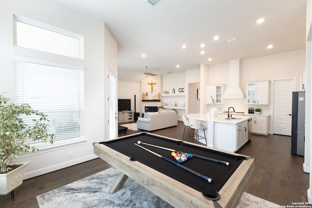 recreation room with a large fireplace, baseboards, dark wood finished floors, recessed lighting, and a sink