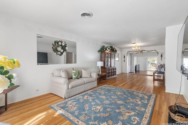 living room featuring a notable chandelier, wood finished floors, visible vents, and baseboards