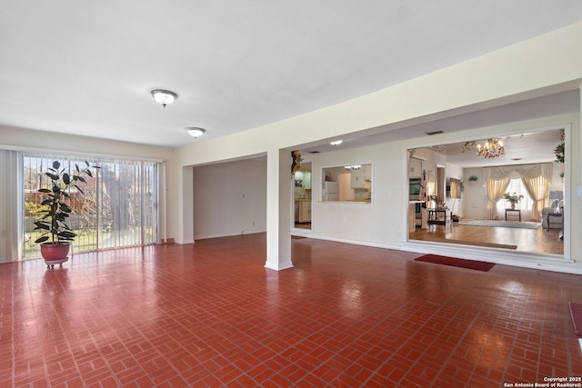 unfurnished living room with a notable chandelier, brick floor, and baseboards