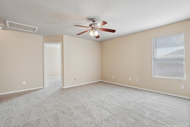 carpeted empty room featuring baseboards, attic access, and a ceiling fan