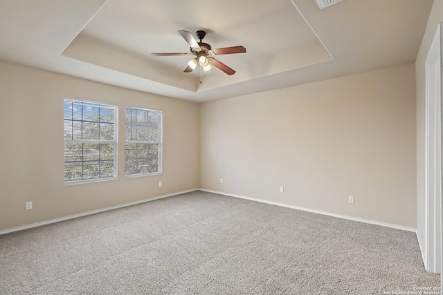 carpeted empty room with visible vents, baseboards, a raised ceiling, and ceiling fan