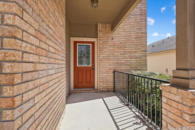 view of exterior entry featuring brick siding and a balcony