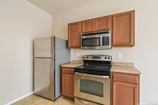 kitchen featuring brown cabinetry, baseboards, light countertops, appliances with stainless steel finishes, and light tile patterned flooring