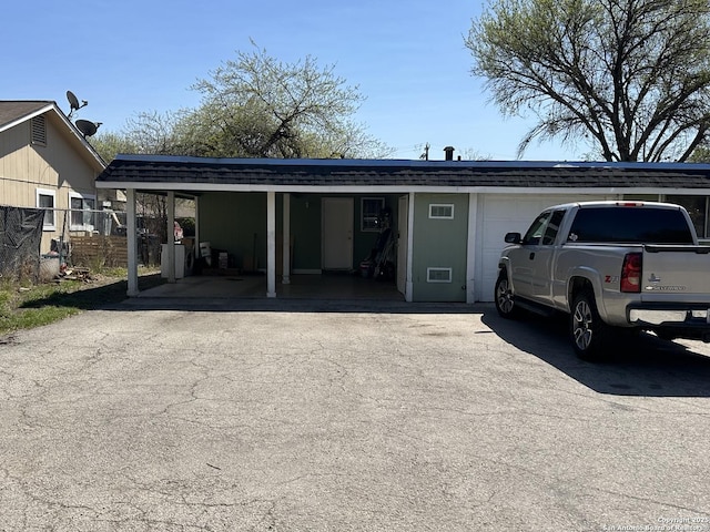 view of front facade with driveway, roof with shingles, and fence