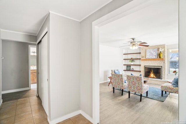 living room with a brick fireplace, crown molding, baseboards, light wood-style floors, and a ceiling fan