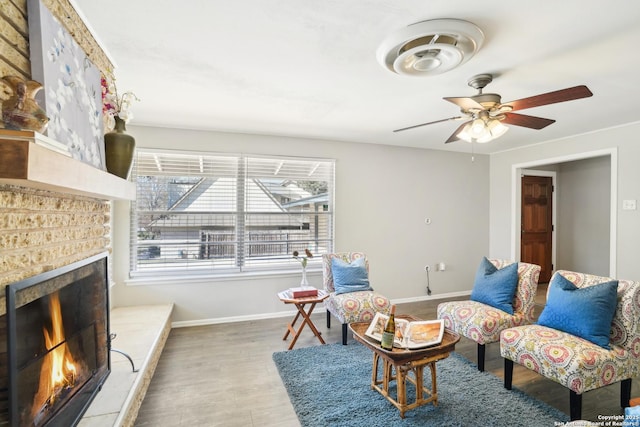 sitting room with a tiled fireplace, wood finished floors, baseboards, and a ceiling fan