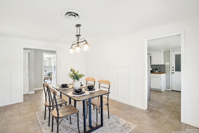 dining space with light tile patterned floors, visible vents, wainscoting, and a decorative wall