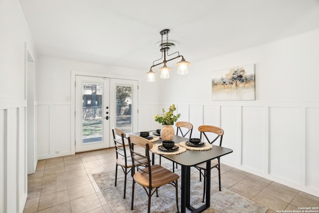 dining area with a decorative wall, light tile patterned flooring, french doors, and a wainscoted wall