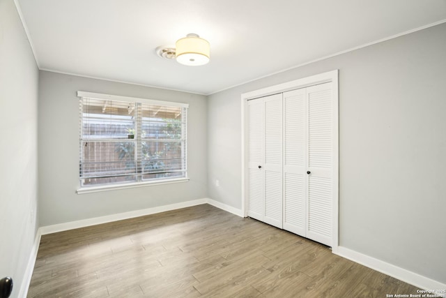 unfurnished bedroom featuring wood finished floors, baseboards, a closet, and ornamental molding