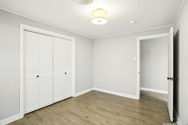 unfurnished bedroom featuring a closet, crown molding, baseboards, and wood finished floors