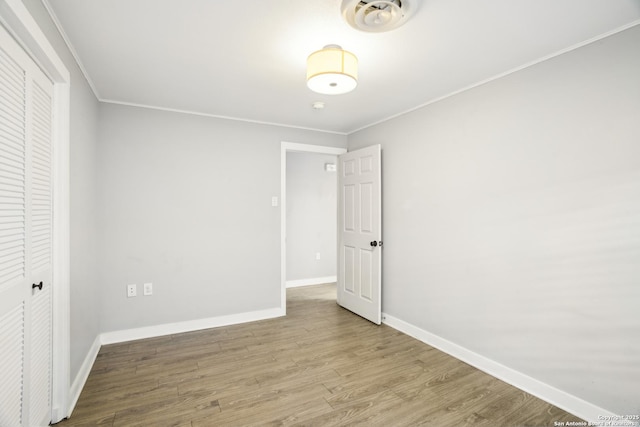 unfurnished bedroom featuring wood finished floors, visible vents, baseboards, ornamental molding, and a closet