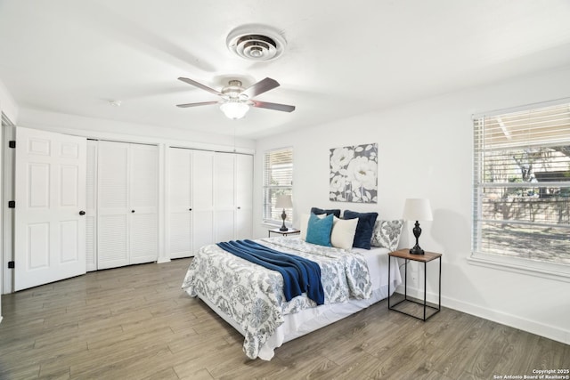 bedroom with wood finished floors, visible vents, two closets, and baseboards