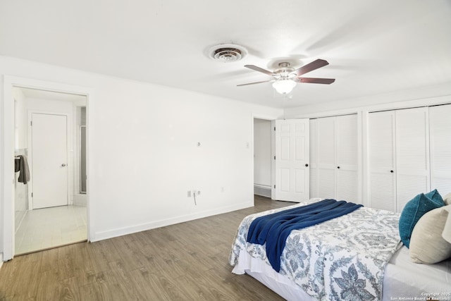 bedroom featuring visible vents, two closets, wood finished floors, baseboards, and ceiling fan