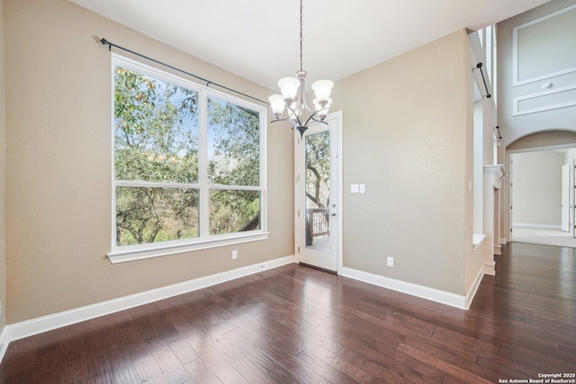 unfurnished dining area with a notable chandelier, wood finished floors, arched walkways, and baseboards