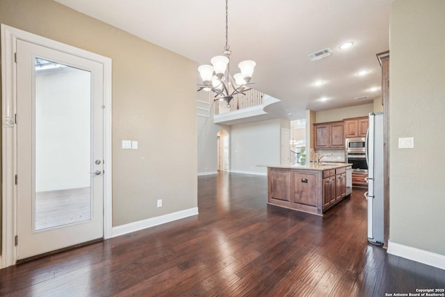 kitchen with visible vents, dark wood finished floors, brown cabinetry, stainless steel appliances, and a kitchen island with sink