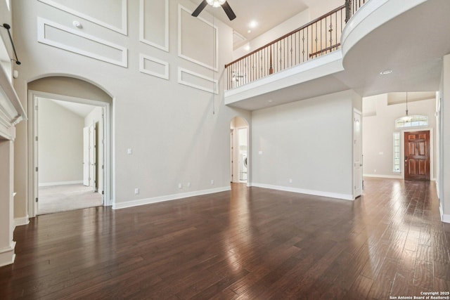 unfurnished living room with a ceiling fan, arched walkways, wood-type flooring, and baseboards