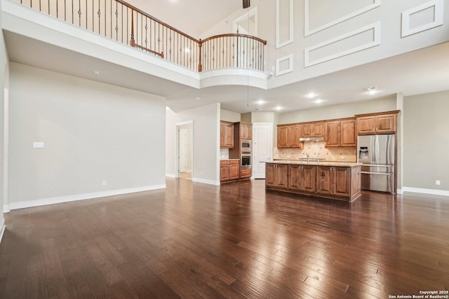 unfurnished living room featuring a sink, baseboards, a high ceiling, and dark wood finished floors