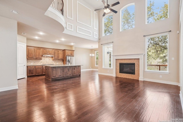 unfurnished living room featuring a glass covered fireplace, ceiling fan with notable chandelier, dark wood-type flooring, and a healthy amount of sunlight