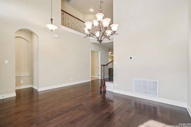 unfurnished room featuring wood finished floors, baseboards, visible vents, arched walkways, and stairs