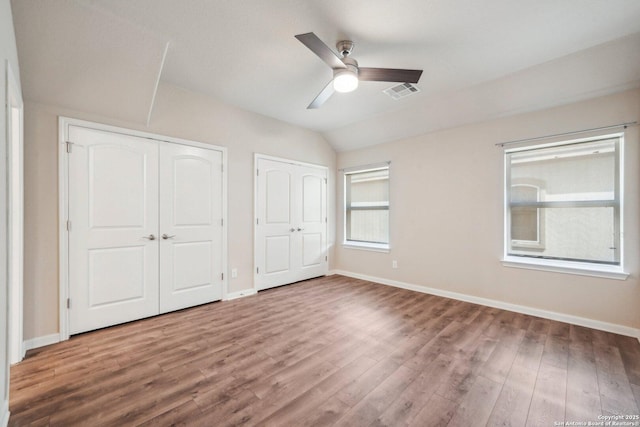 unfurnished bedroom featuring visible vents, wood finished floors, multiple closets, and vaulted ceiling