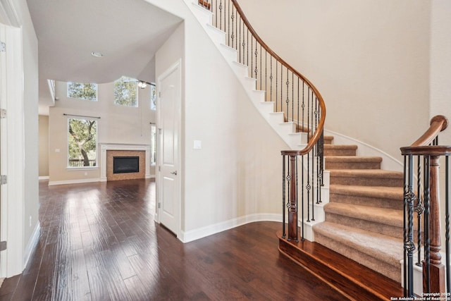 staircase featuring hardwood / wood-style floors, a glass covered fireplace, a high ceiling, and baseboards