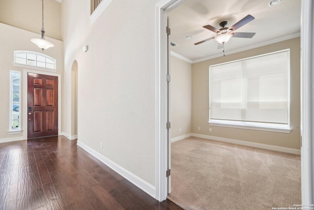 entrance foyer featuring baseboards, ornamental molding, arched walkways, a ceiling fan, and dark wood-style flooring