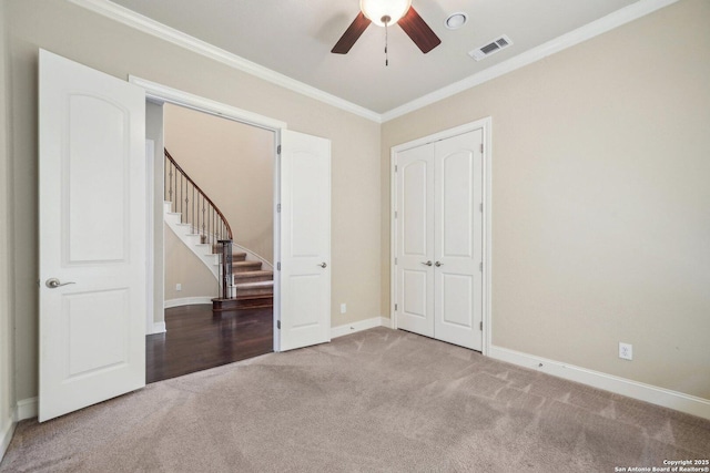 carpeted spare room featuring stairway, a ceiling fan, baseboards, visible vents, and crown molding