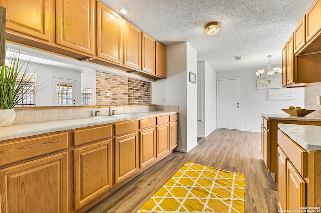 kitchen with visible vents, a sink, wood finished floors, light countertops, and decorative backsplash