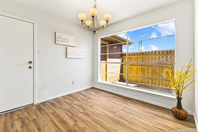 unfurnished dining area featuring baseboards, a notable chandelier, wood finished floors, and a textured ceiling