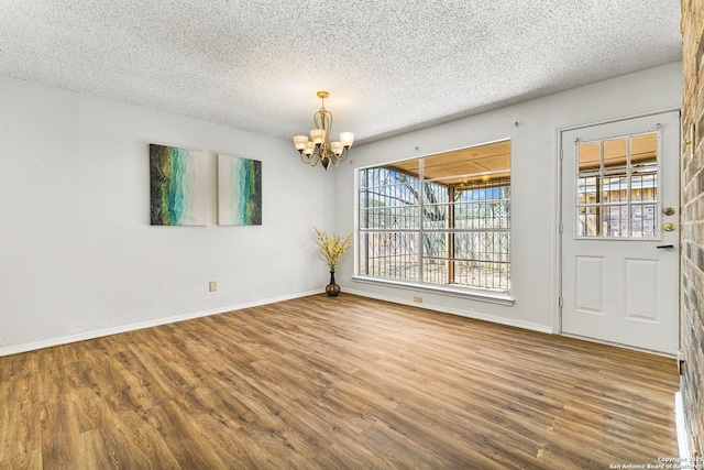 unfurnished room featuring baseboards, a notable chandelier, wood finished floors, and a textured ceiling