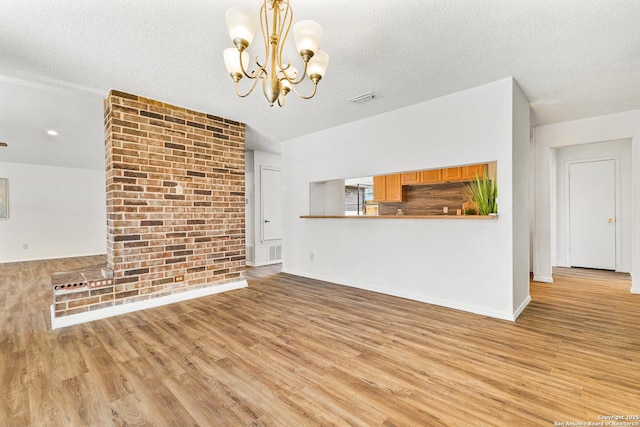 unfurnished living room featuring a textured ceiling, wood finished floors, visible vents, and a chandelier